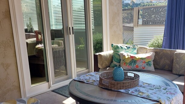 A sunlit patio area with a round table, wicker furniture, and a view through a glass door. - Private Home great single story home. Plenty of space for the family. (San Diego)