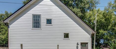 A small, single-story white building with a gabled roof, a front door, and a small window.
