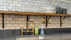 Una cocina con encimera de granito, pileta de acero inoxidable y muebles de color negro. Hay repisas sobre la pileta con vasos y platos.