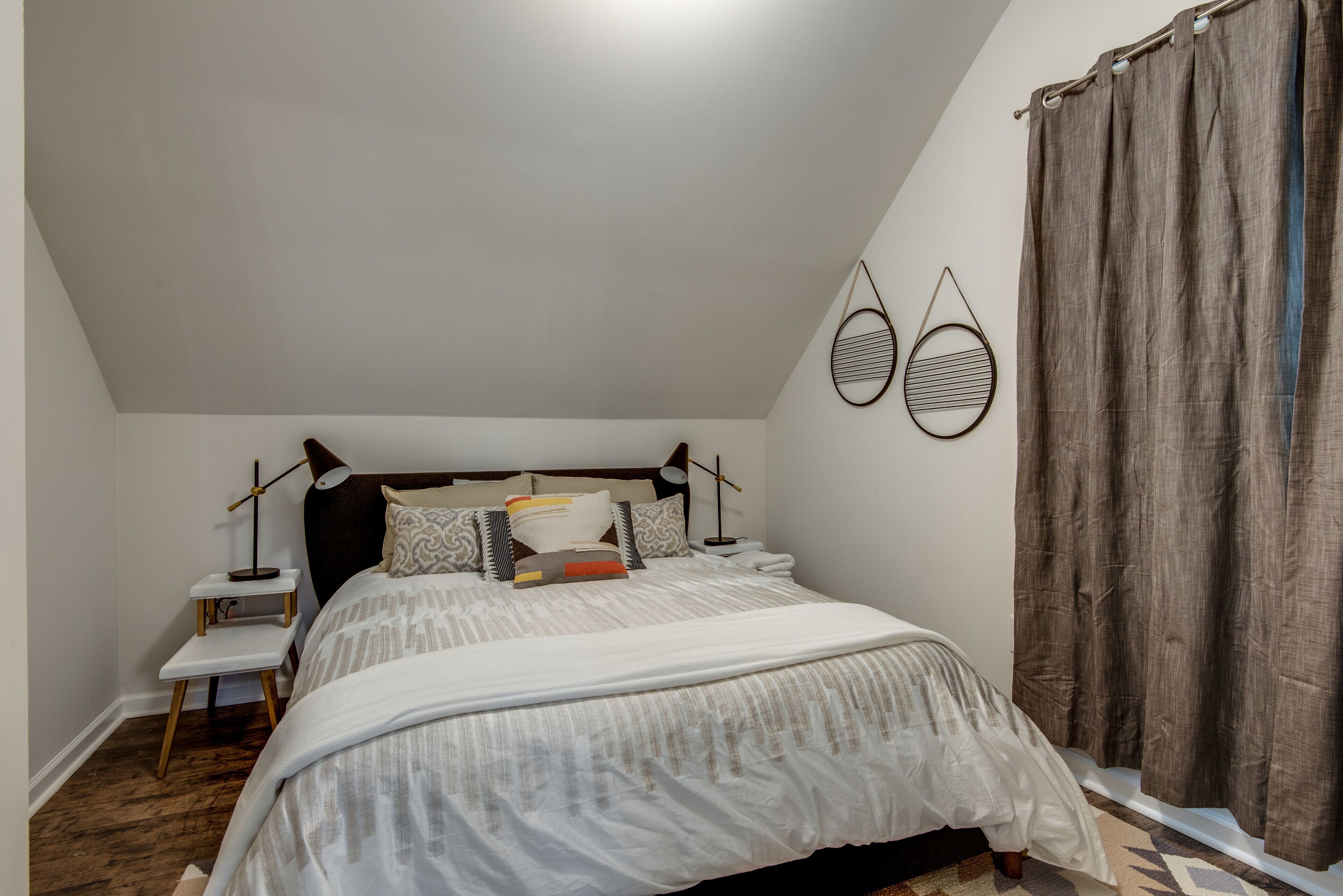 Une chambre à coucher avec un lit, des tables de chevet, une commode, une lampe et un rideau.