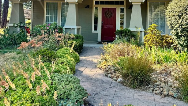 A two-story house with a red front door, a covered porch, and a well-maintained garden with various plants and shrubs.