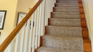 A staircase with a wooden handrail, carpeted steps, and a ceiling fan.