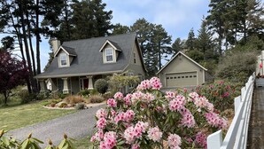 A two-story house with a grey roof, a front porch, and a driveway leading to a garage.