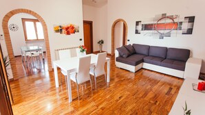 A modern living room with a sectional sofa, a dining area with a white table and chairs, and a kitchen visible through an archway. - Large appartment near the Airport, private free parking (Fiumicino)