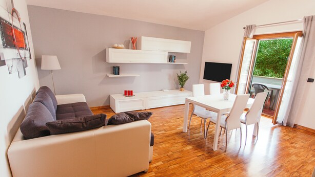 A modern living room with a sofa, dining table, chairs, a TV, and a balcony with a view. - Large appartment near the Airport, private free parking (Fiumicino)