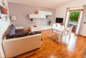 A modern living room with a sofa, dining table, chairs, a TV, and a balcony with a view. - Large appartment near the Airport, private free parking (Fiumicino)