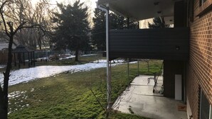 Een achtertuin van een woonhuis met een overdekt terras, een bakstenen huis en een gazon met enkele sneeuwplekken.
