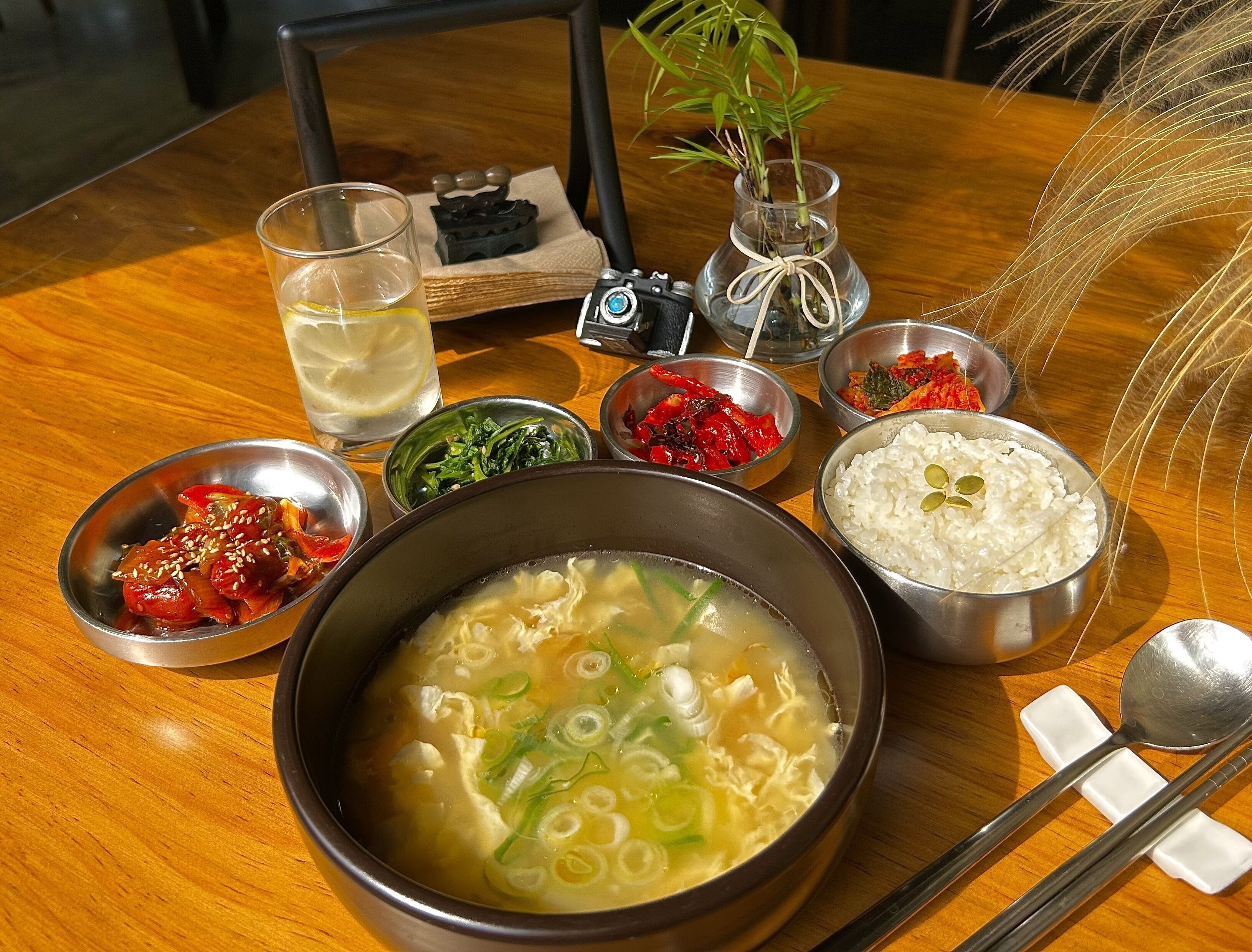 Una mesa con varios platos, incluyendo un tazón de sopa, tazones de acompañamientos y un vaso de agua.