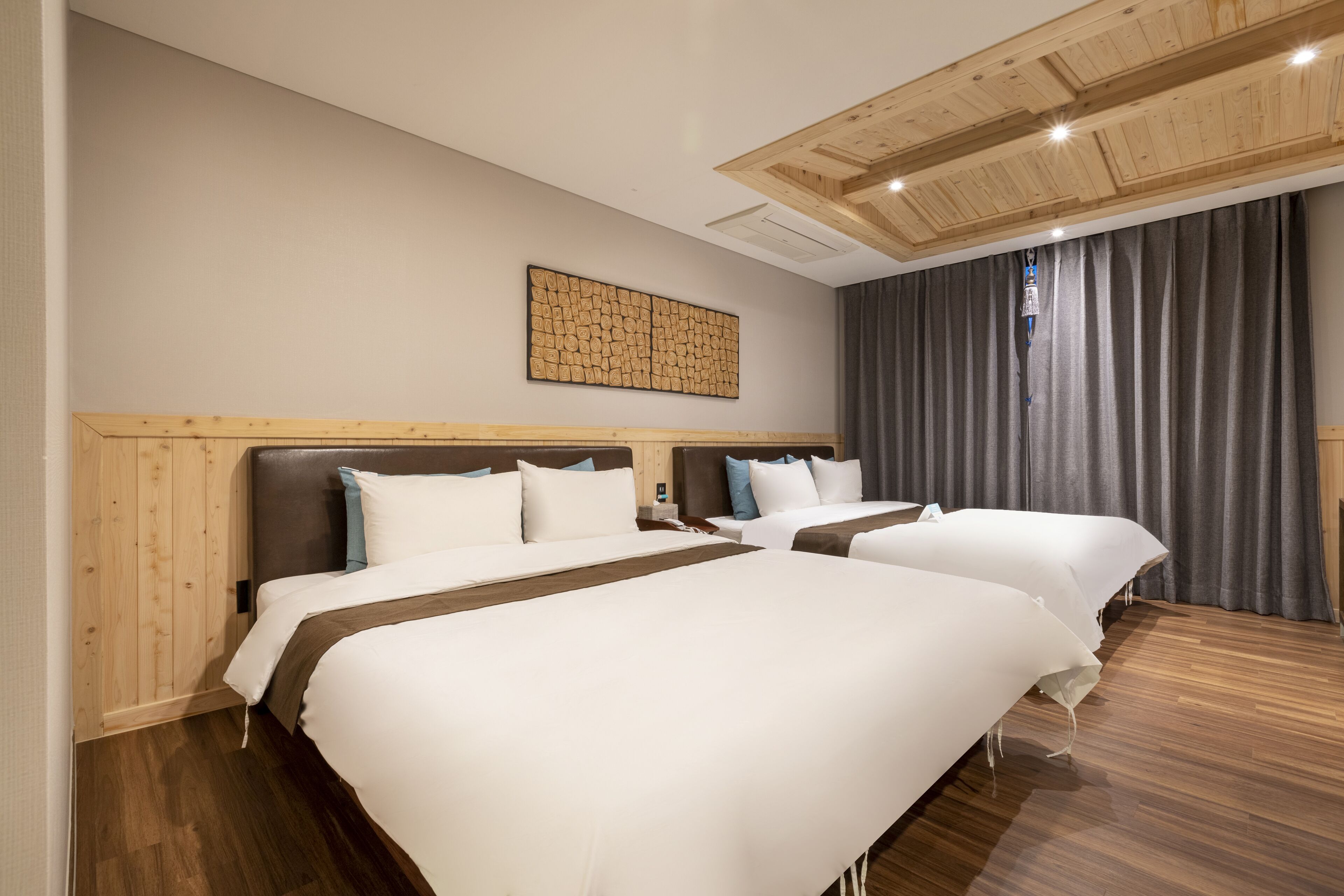 A hotel room with two beds, wooden headboards, a large abstract artwork on the wall, and a grey curtain.