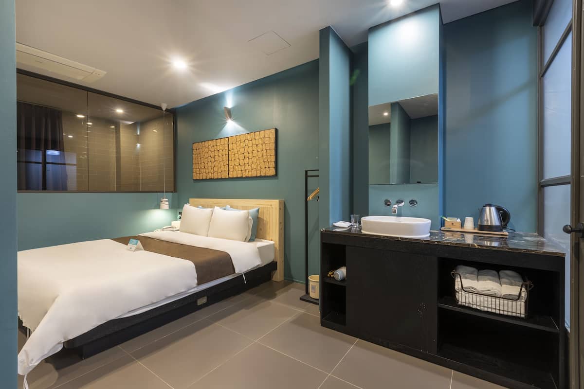 A modern hotel room with a single bed, a vanity with a mirror, and a built-in shelf with towels.
