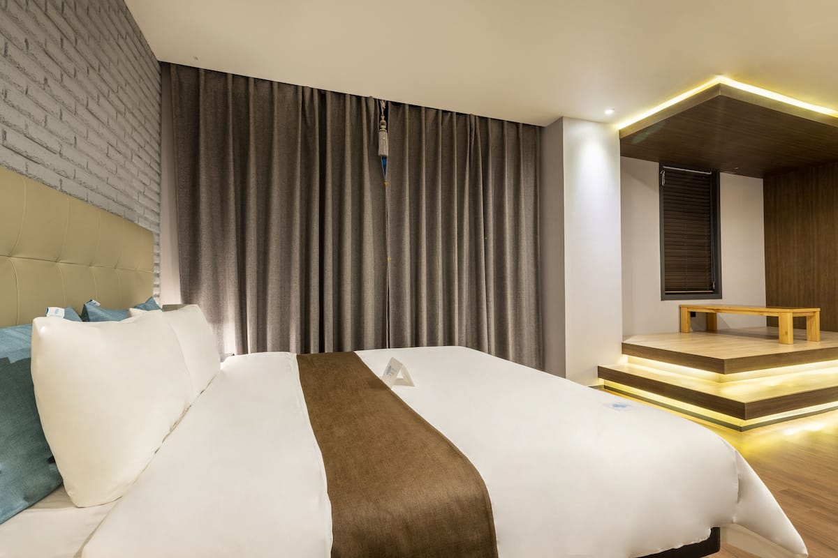 A modern hotel room with a large bed, a headboard, a wooden bench, and a staircase leading to a balcony.