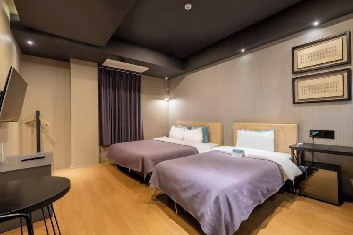 A hotel room with two beds, a desk, a chair, and a TV.