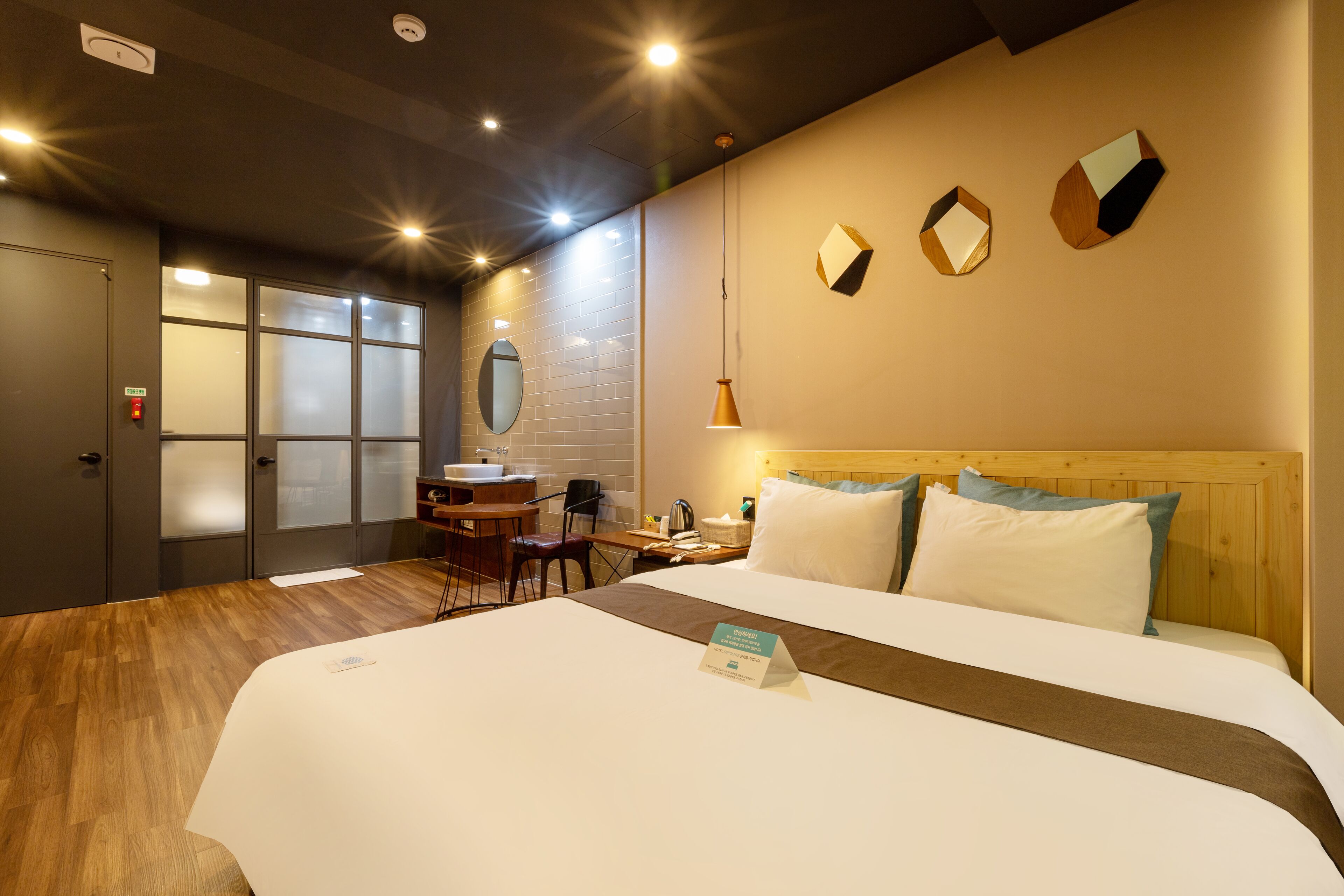 Une chambre d’hôtel avec un grand lit, un bureau avec une chaise, un miroir et une fenêtre à vitre dépolie.