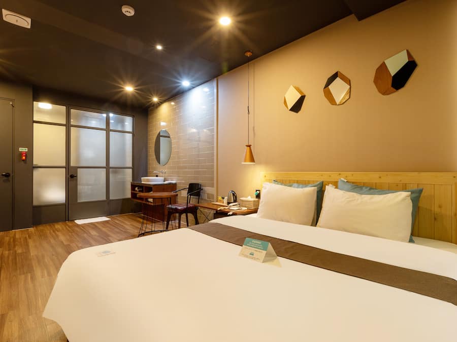 Une chambre d’hôtel avec un grand lit, un bureau avec une chaise, un miroir et une fenêtre à vitre dépolie.