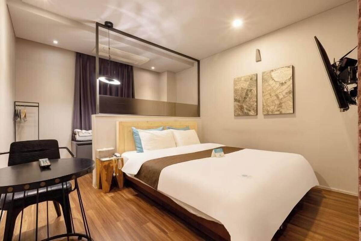 A hotel room with a bed, a desk, a chair, a mirror, and artwork on the wall.