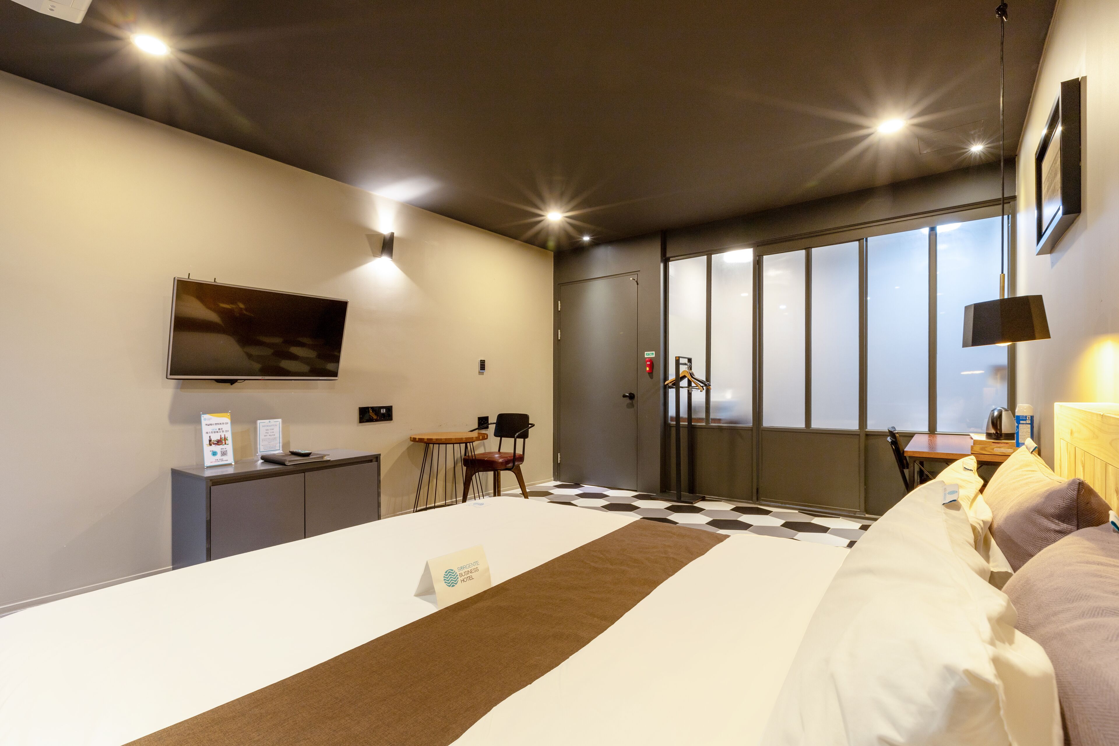 A hotel room with a large bed, a desk, a chair, a television, and a window with blinds.