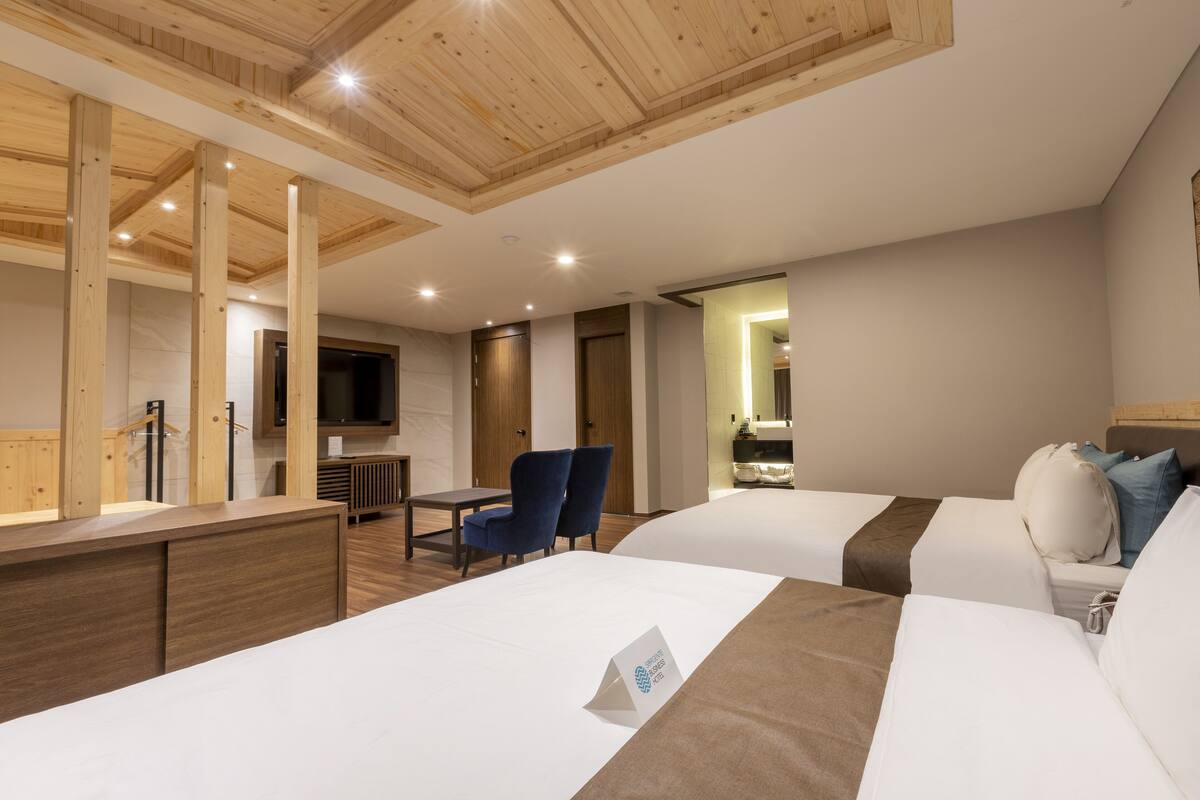 A hotel room with two beds, a desk, chairs, and a TV.