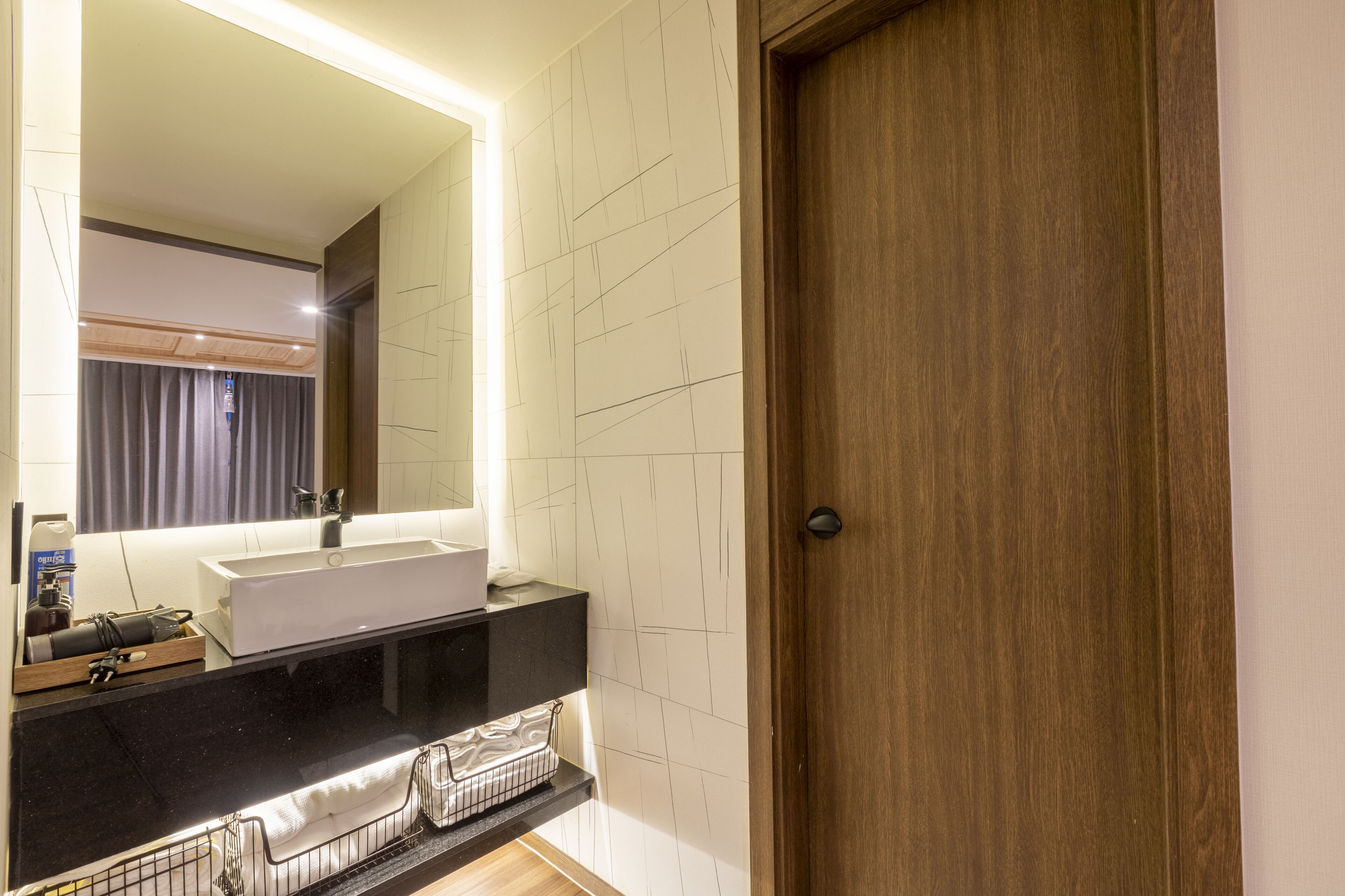 A modern bathroom with a large mirror, a white sink, and a wooden door.