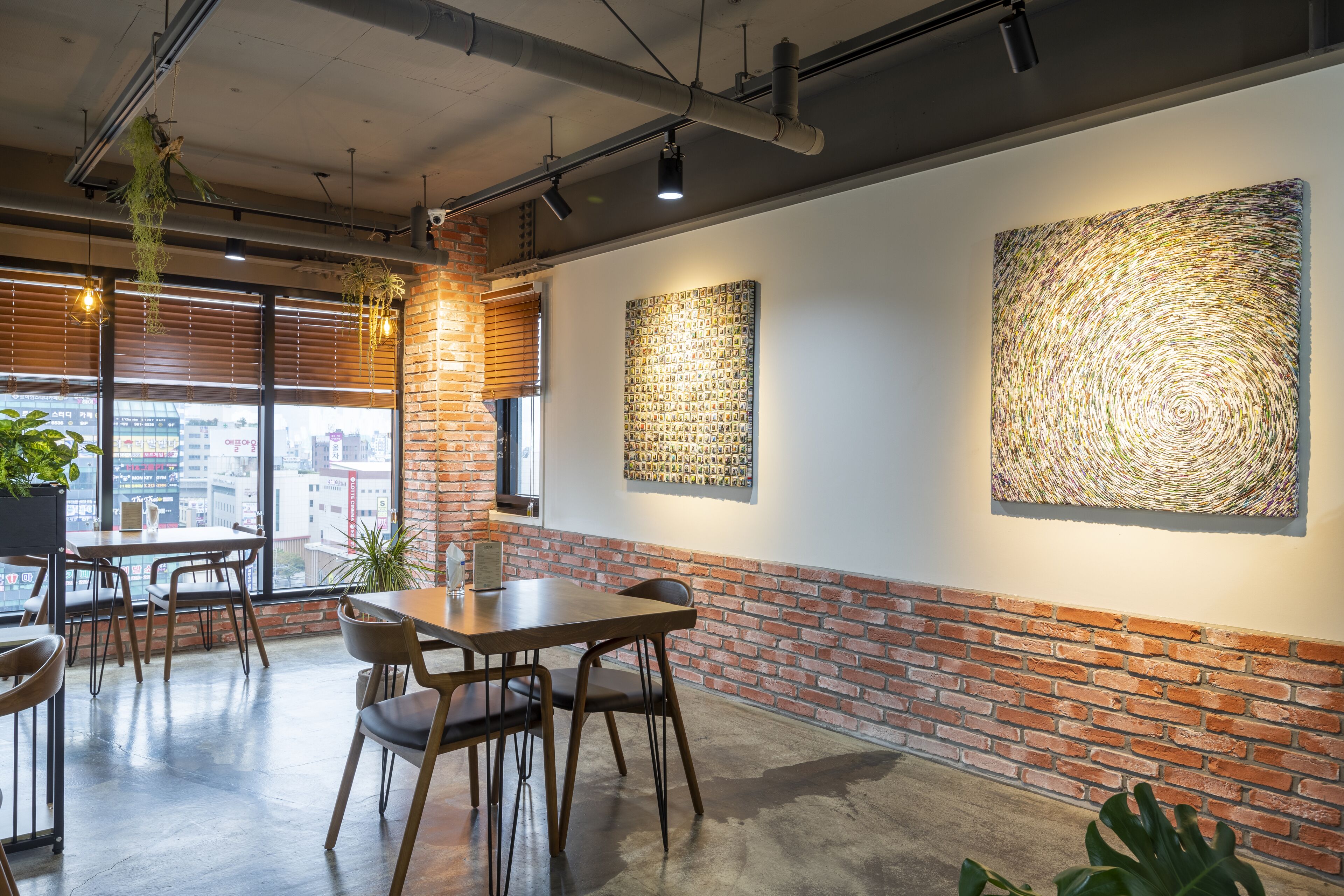A modern interior with exposed brick walls, wooden tables, and hanging plants.