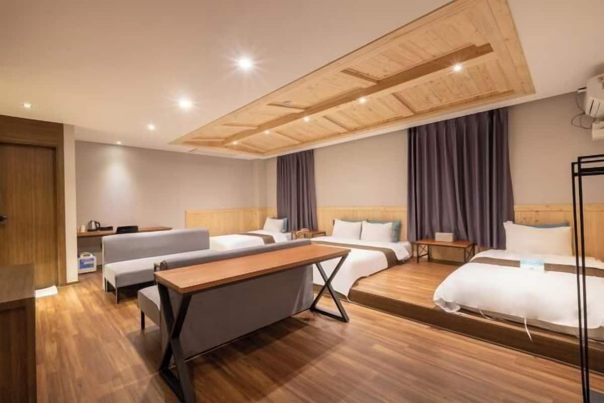 A hotel room with a wooden ceiling, two beds, a desk, and a sofa.