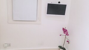 A room with a white door, a small potted orchid, a laptop on a white fluffy bed, and a Vogue magazine on the floor. - The studio - the heart of Primrose Hill (London)