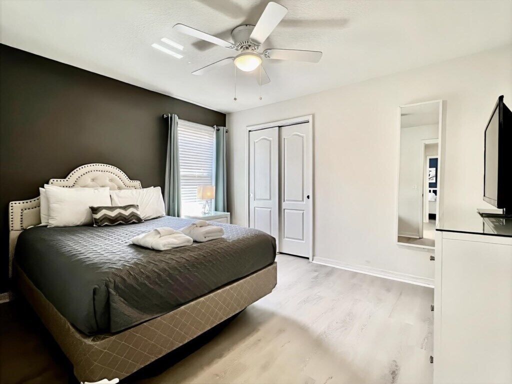 Une chambre à coucher comprenant un lit, un ventilateur de plafond, un radiateur, une porte et un téléviseur.
