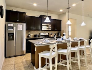 A modern kitchen with dark cabinets, stainless steel appliances, a granite countertop, and white bar stools.