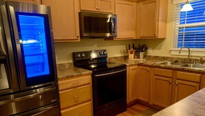 A kitchen with stainless steel appliances, wooden cabinets, granite countertops, and a window with blinds.