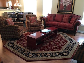 A living room with a red sofa, patterned armchairs, a coffee table, and a large rug. - Elegant & Tranquil 3BR Townhome in Greenville’s Convention District (Greenville)