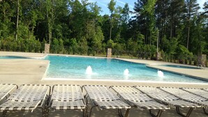 A swimming pool with a fountain, surrounded by lounge chairs and trees.