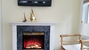 A living room with a fireplace, a mounted TV, and a wicker chair. - Very Clean, Well-appointed Cottage (Lakeside Marblehead)