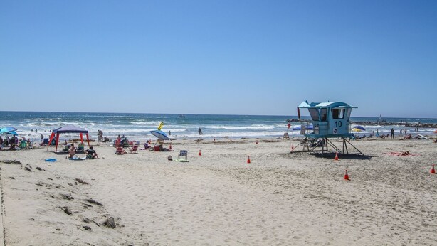 Une plage avec des postes de surveillance pour les sauveteurs, des chaises longues, des parasols et des gens qui se détendent.