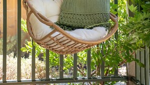A wicker hanging chair with a cushion and a knitted pillow, set against a backdrop of lush greenery. - Discover the Perfect Wine Country Getaway 2Bed 2Bath (Paso Robles)