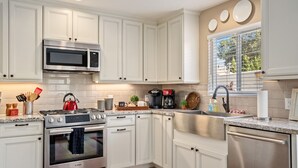 A modern kitchen with white cabinetry, stainless steel appliances, a kettle, a coffee maker, and a window with blinds. - Discover the Perfect Wine Country Getaway 2Bed 2Bath (Paso Robles)