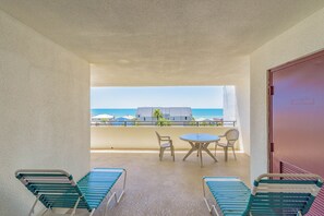 Een balkon met een tafel en stoelen, met uitzicht op een strand met gebouwen en een heldere lucht.