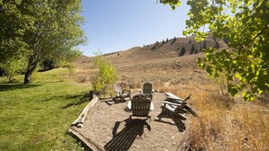 Eine Außenbereich-Sitzgelegenheit mit Adirondack-Stühlen und einer Holzterrasse, umgeben von Bäumen und einer hügeligen Landschaft.