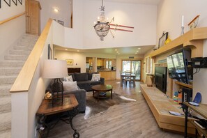 Relax in a spacious living area with a high ceiling, featuring a comfortable seating area, flat-screen TV, and dining table with a view of the outdoors.