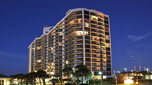 A multi-story hotel with balconies, a pool area, and a well-lit facade.