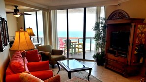 Un salon comprenant un canapé, des fauteuils, une table basse, un téléviseur et un balcon avec vue sur l’océan.