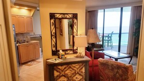 Une chambre d’hôtel avec un coin cuisine, un grand miroir, un canapé rouge, une table avec une lampe et une vue sur la mer.