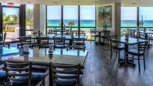 Un restaurant doté de nombreuses tables et chaises, de grandes fenêtres donnant sur l’océan et d’un panneau indiquant la sortie.