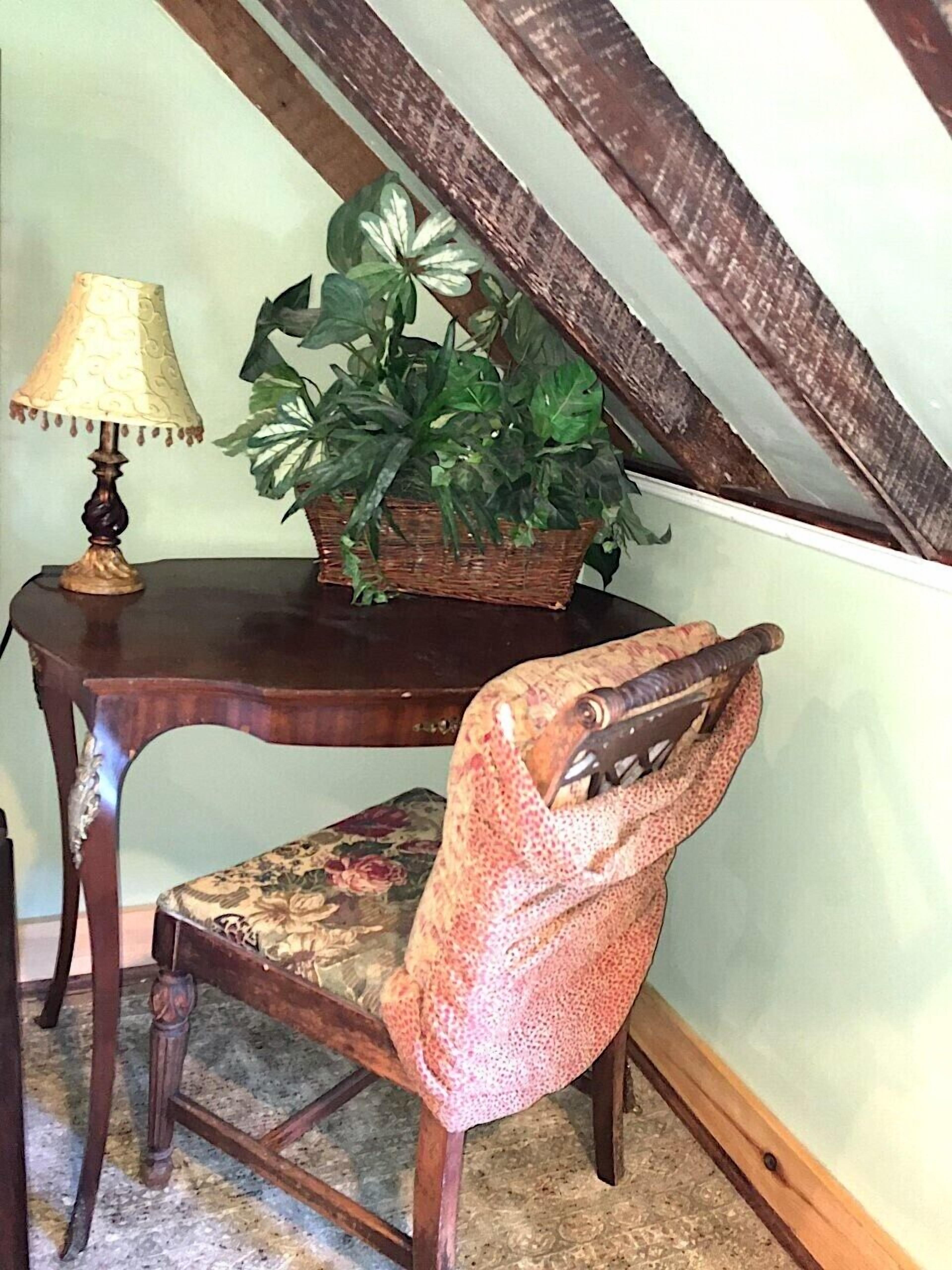 Een houten stoel met een bloemenkussen, een rieten mand met een plant en een tafellamp.