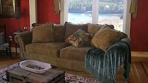 A cozy living room with a brown sofa, a small table, and a view of a lake through a large window.