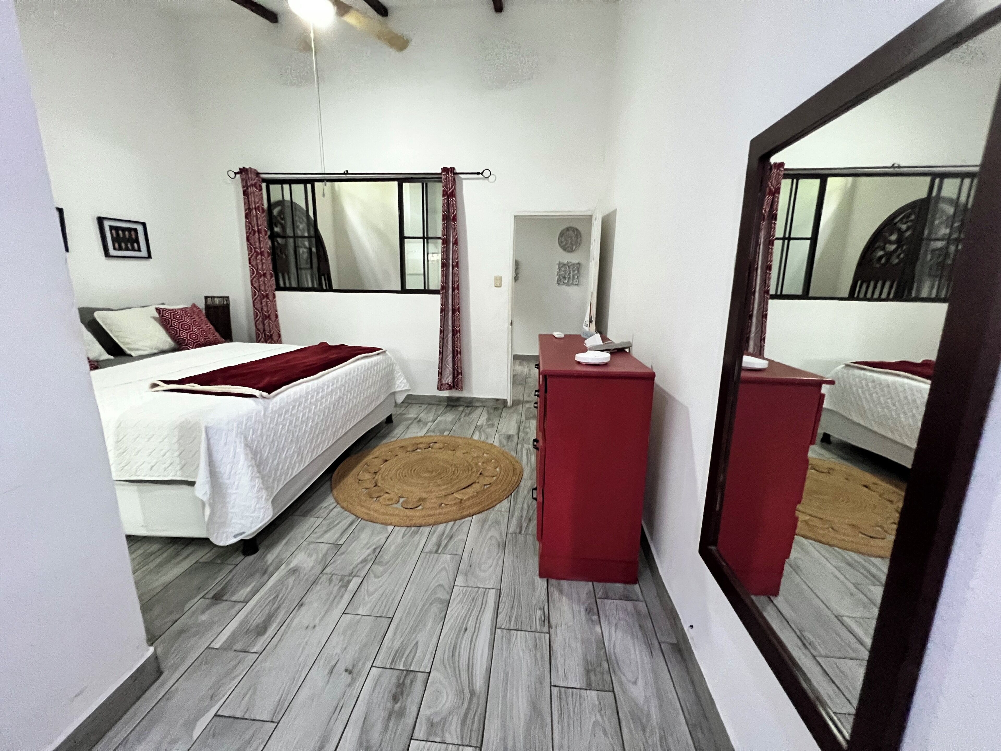 Un dormitorio con cama, cómoda, espejo y ventana con cortinas.