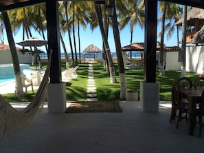 A covered outdoor area with a pool, lounge chairs, a hammock, and a view of the ocean and palm trees. - Beachfront House In Exclusive Beach (Cangrejera,)