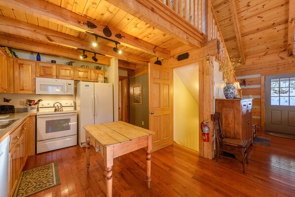 A wooden cabin interior with a kitchen, dining table, and a cozy fireplace area. - Pet-Friendly Cabin in Seven Devils (Seven Devils)