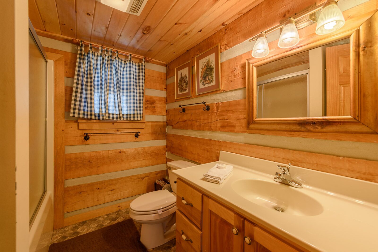 A wooden-paneled bathroom with a white sink, a toilet, and a mirror above the sink.