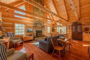 A log cabin interior with a stone fireplace, wooden furniture, and large windows. - Pet-Friendly Cabin in Seven Devils (Seven Devils)
