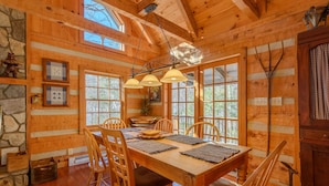 Una cabaña de madera con comedor, que incluye una mesa grande, sillas y una lámpara colgante.