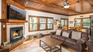 Ein Wohnzimmer mit Kamin, Ledersofa, Couchtisch aus Holz und großen Fenstern.